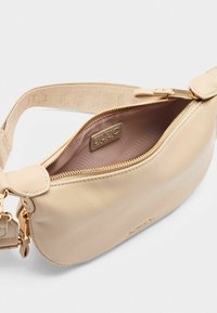 Borsa in pelle beige con apertura con zip, superficie testurizzata e hardware in tonalità oro. La tracolla in tessuto regolabile presenta un dettaglio con logo.