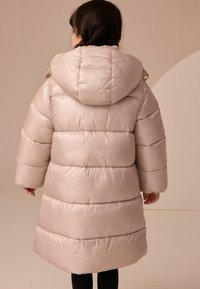 Puffig beige barnjacka med huva, med horisontell sömnad och stora ärmar. Slät, glansig yta med knappdetaljer.