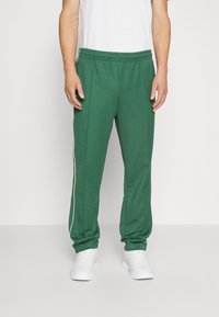 Green athletic pants with a drawstring waistband, side white stripes, and tapered legs. Made of soft, textured fabric.