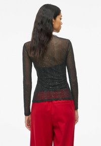 Top negro de manga larga con un diseño transparente y destellos plateados, con una cintura ajustada. Textura suave y un ligero fruncido en el dobladillo.