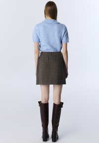 Lichtblauwe korte mouw sweater met een kraag, gecombineerd met een bruin geruit mini-jurk. Bruine leren laarzen tot de knie met vierkante hakken.