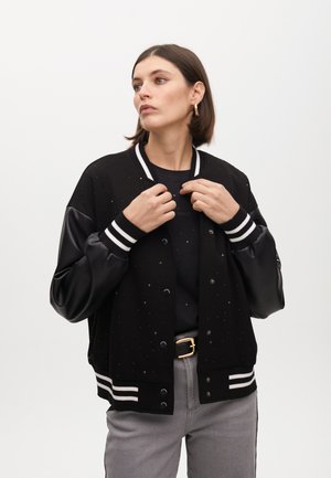 Black varsity jacket with shiny studs, sport collar, and leather sleeves. Features striped ribbed cuffs and waistband, finished with snap buttons.