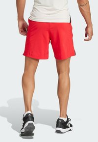 Shorts de sport rouges en tissu léger, avec un design simple agrémenté d'un accent noir sur le côté et une taille élastique confortable.