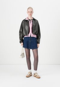 Lærbomberjakke med rosa krage, pastelrosa cardigan, denimskjørt, beige mønstrede sneakers og en liten hvit håndveske.