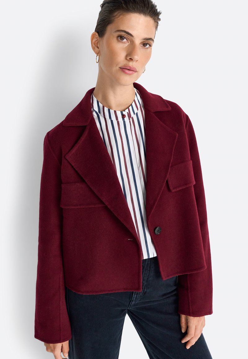 Burgundy wool-blend cropped jacket with notched lapels, two front pockets, and a single black button. Paired with a striped blouse.