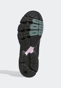 Černá sportovní podrážka s texturovaným vzorkem, s úpravami v zelené a růžové barvě. Zaměření na prvky designu zajišťující trakci a tlumení.