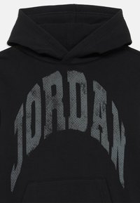 Čierna mikina s kapucňou s veľkým šedým grafickým potlačou "JORDAN" v poškodenom dizajne cez hruď, s mäkkou textúrou.