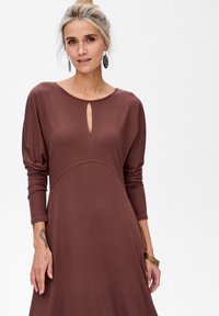 Robe longue marron à manches longues avec un col rond et un détail en trou de serrure. Tissu doux avec une texture lisse, corsage ajusté et jupe évasée.