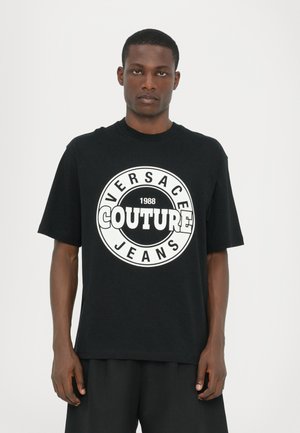 Svart bomull t-skjorte med et stort hvitt logo som har "VERSACE COUTURE JEANS" og "1988." Korte ermer og en avslappet passform.