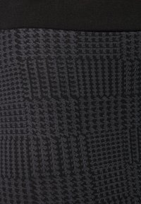 Leggings noirs texturés ornés de divers motifs géométriques. La taille est entièrement noire et élastiquée pour un maintien sûr.