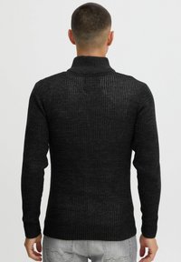 Sort strikket sweater med høj krave, ribbet tekstur og lange �ærmer. Stoffet har et subtilt mønster og en tætsiddende silhuet.