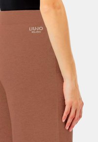 Leggings in maglia marrone con una texture morbida, dotati di un'alta vita e del logo "LIU JO MILANO" in bianco sul davanti.