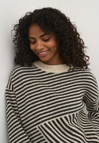 Pull en tricot rayé crème et marine, avec des rayures horizontales et un col à côtes. Texture douce, coupe décontractée et design à épaules tombantes.