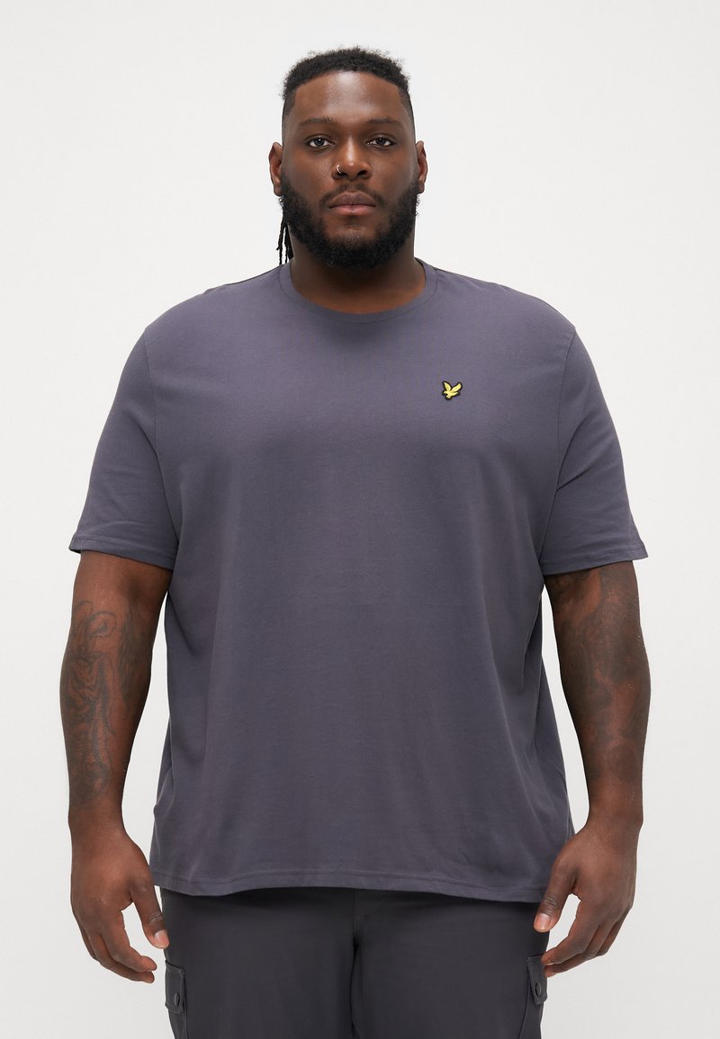 Dunkelgraues Baumwoll-T-Shirt mit kurzen Ärmeln, rundem Ausschnitt und einem kleinen gelben gestickten Logo auf der linken Brust. Glatte Textur.