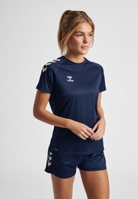 Navy athletic shirt with short sleeves, featuring a logo and chevron pattern on the shoulders. Paired with matching shorts. Smooth texture.