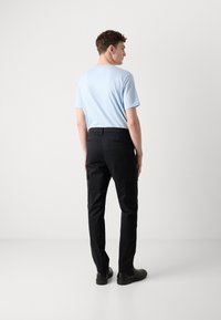 Lichtblauw T-shirt en zwarte cargobroek met zijzakken en een slim fit, rustend op zwarte schoenen tegen een effen achtergrond.