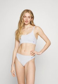 Jasnoszary sportowy biustonosz i dopasowany strój bikini wykonane z miękkiej tkaniny, z fioletowymi akcentami logo i prostym, nowoczesnym designem.