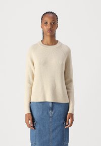 Μπεζ ριγωτό πλεκτό πουλόβερ με στρογγυλή λαιμόκοψη και μακριά μανίκια, συνδυασμένο με τζιν φούστα με τσέπες cargo και άνετη εφαρμογή.