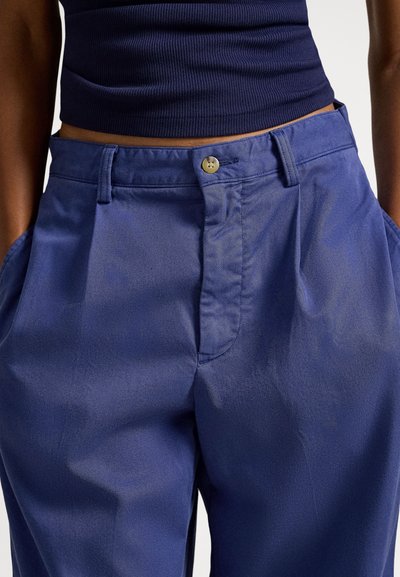 Niebieskie lekkie spodnie o gładkiej fakturze, z zapięciem na guzik, płaskim przodem i bocznymi kieszeniami.