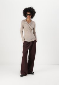 Beige långärmad omslagstopp i texturerad tyg, matchad med vida mörkbruna byxor. Svarta skräddarsydda skor fulländar outfiten.