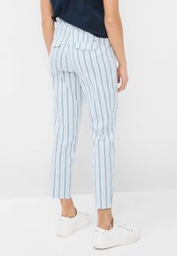 Pantalons rayés bleu et blanc ajustés, avec une taille mi-haute, des poches arrière et une longueur cropped, associés à des baskets blanches.