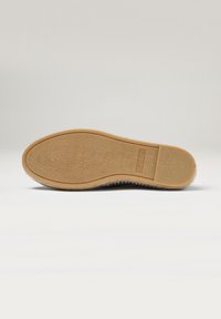 Suela de goma con una superficie texturizada. El borde presenta un contorno suave. El color es marrón claro con un ligero grano, lo que indica durabilidad y agarre.
