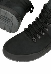 Scarpe da trekking nere in suede e mesh, dotate di una suola in gomma grigia robusta con una superficie strutturata per una presa migliore e lacci neri con occhielli in plastica.