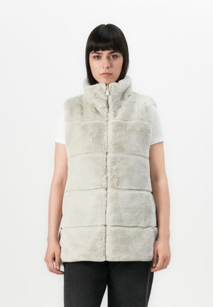 Grijze nepbont vest met hoge kraag, rits aan de voorkant en gequiltte panelen. Ggedragen over een wit shirt met een zachte, gestructureerde oppervlakte.