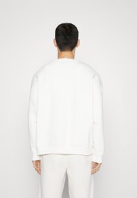Sudadera blanca de corte holgado, con cuello redondo y puños de canalé. Textura suave y diseño minimalista, sin logotipos visibles.