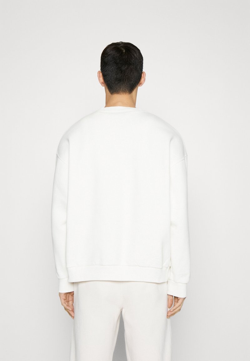 Sudadera blanca de corte holgado, con cuello redondo y puños de canalé. Textura suave y diseño minimalista, sin logotipos visibles.