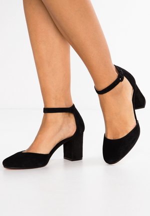 Black suede high-heeled shoes with a rounded toe, ankle strap, and block heel. Open sides with a smooth texture.