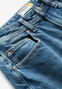 Vaqueros de denim azul de corte bootcut relajado, con una sutil textura, costuras en color cobre y un pequeño bolsillo frontal con un detalle de remache metálico.