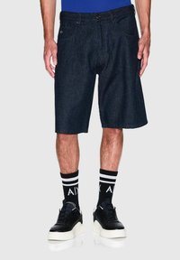 Shorts in denim scuro con una vestibilità rilassata, tasche anteriori e un logo sottile. Indossati con sneaker nere e calzini a righe neri.