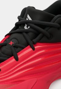 Primo piano di una scarpa sportiva nera e rossa con suola spessa e texture, lacci neri e logo sulla linguetta.