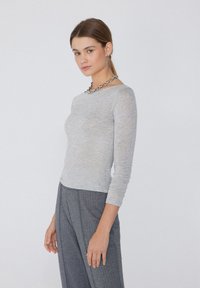 Graues Langarmshirt in taillierter Form, aus weichem Material, kombiniert mit gemusterten grauen Hosen. Hat einen einfachen Rundhalsausschnitt.