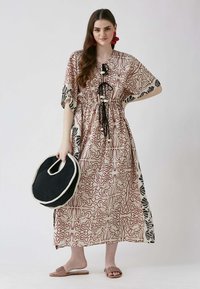 Maxime dress in beige with abstract red and black patterns, short sleeves, cinched waist, and a tie detail. Paired with a black round bag.