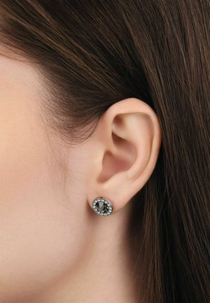Nahaufnahme eines Frauenohres mit glattem braunem Haar, das einen runden silbernen Ohrring mit einem zentralen schwarzen Stein umgeben von klaren Kristallen trägt.