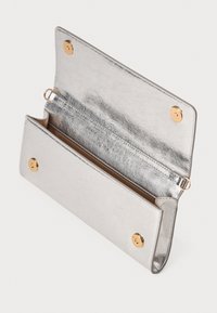 Clutch in metallo argentato con apertura a portafoglio, bottoni a pressione dorati e tracolla removibile su sfondo bianco.