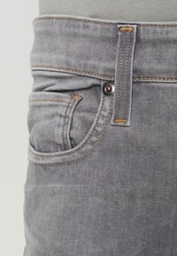 Jeans de mezclilla gris con un bolsillo frontal con costuras naranjas en contraste. La tela tiene una textura suave y un corte clásico.