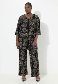 Musta kukkakuosinen asu, jossa on polvea hipova takki, jossa on kolmivartiset hihat ja leveälahkeiset housut, molemmat beigen värisin ruusukuviin.