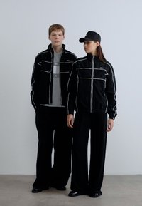 Μαύρα σακάκια με λευκές ραφές, φορεμένα πάνω από γκρι μπλουζάκια. Χαλαρό μαύρο παντελόνι και μαύρο καπέλο ολοκληρώνουν την μινιμαλιστική, αθλητική εμφάνιση.