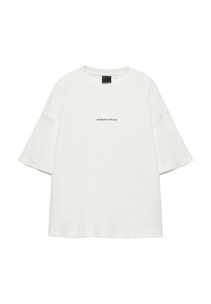 T-shirt blanc à manches courtes oversize avec texte noir "THE BEAUTY OF THE BLUR" centré sur la poitrine et col rond.