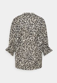 Rückansicht einer locker sitzenden Bluse mit einem schwarz-weißen abstrakten Muster, weichem Material und hochgerollten Ärmeln.