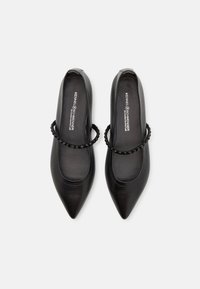 Ballerines noires à bout pointu avec des brides décoratives cloutées sur le dessus, étiquetées « Kennel & Schmenger » sur la semelle intérieure.