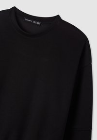 Felpa nera a maniche lunghe con scollo rotondo, texture morbida e design minimale. Etichetta visibile con il nome del marchio "Terranova."
