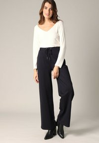 Witte geribbelde langemouwen top met V-hals, gecombineerd met marineblauwe broek met streepjes en een losse pasvorm, voorzien van een koord in de taille en zwarte enkellaarsjes.