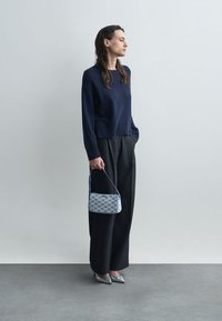 Námornícky pletený sveter, voľné čierne nohavice a modro-biele vzorované kabelka. Strieborné špicaté topánky dopĺňajú outfit.