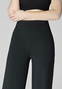 Czarne, wysokie spodni o szerokich nogawkach, wykonane z gładkiego, elastycznego materiału. Posiadają bezszwowy pas i czysty, dopasowany krój.