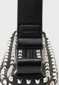 Czarna skórzana torebka z srebrnymi piramidalnymi ćwiekami, z szerokim paskiem i metalowym zapięciem. Gładka textura i uporządkowany design.