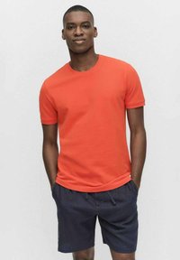 Ljust orange bomulls t-shirt med rund hals och korta ärmar, kombinerad med marinblå shorts. Slät textur med en avslappnad passform.